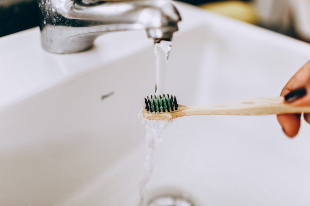 pexels photo 27176875 Eco-friendly bamboo toothbrush under running water from faucet in a bathroom sink.